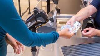 Eine Frau bezahlt mit Bargeld an einer Kasse (Symbolbild)