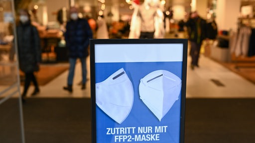 Am Eingang eines Bekleidungsgeschäftes ist ein Hinweisschild mit der Aufschrift "Zutritt nur mit FFP 2-Maske" aufgestellt (Symbolbild)