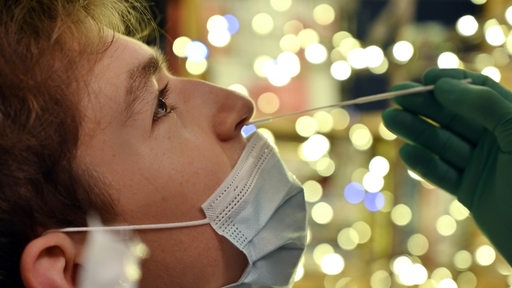 Einem junger Mann wird ein Teststäbchen in die Nase eingeführt, der Hintergrund ist weihnachtlich beleuchtet.