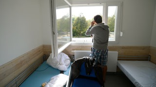 Ein syrischer Flüchtling steht in einer Unterkunft am Fenster und schaut nach draußen (Archivbild)