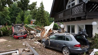 Verwüstungen durch Hochwasser, rund um ein Wohnhaus. in dem Chaos liegen unter anderem zwei Autos.