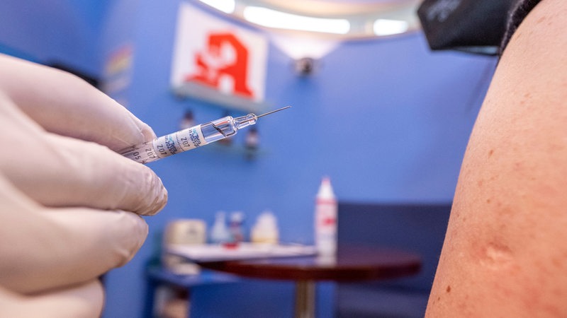 Apotheker  hält nah an dem Arm einer Kundin eine Spritze mit Impfstoff (Archivbild)