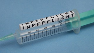 Eine Spritz mit Würfeln, die das Wort "Impfpflicht" zeigen (Symbolbild)