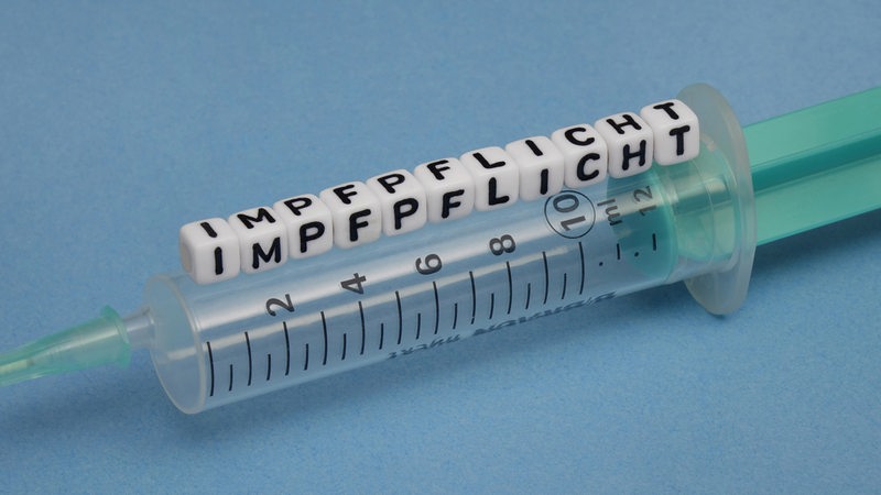 Eine Spritz mit Würfeln, die das Wort "Impfpflicht" zeigen (Symbolbild)