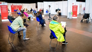 Menschen sitzen im Wartebereich des Impfzentrums in der Messehalle in Bremen