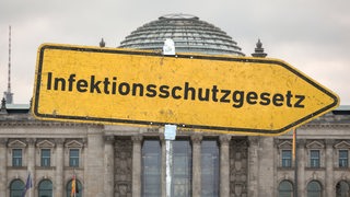 Gelbes Hinweisschild mit der Aufschrift "Infektionsschutzgesetz" vor dem Berliner Reichstagsgebäude (Symbolbild)