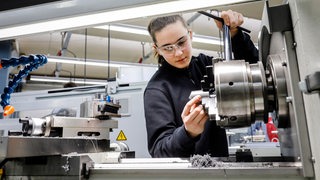 Frau mit Schutzbrille arbeitet an einer Werkzeugmaschine (Symbolbild)