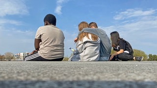 Jugendliche während der Pandemie. Eine Gruppe von Jugendlichen sitzt zusammen auf einer Mauer