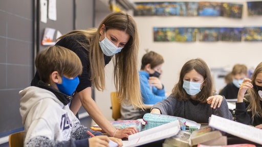 Eine Lehrerin mit Schutzmaske erklärt Kindern mit Schutzmaske eine Aufgabe