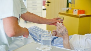 Eine Krankenpflegerin reicht einem Patienten ein Glas Wasser. (Symbolbild)