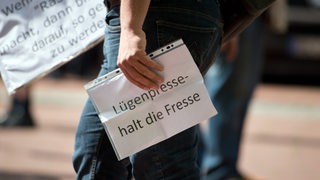 Ein Demonstrant hält einen Zettel mit "Lügenpresse, halt die Fresse" während einer Demonstration (Archivbild)