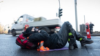 Ein Transporter fährt hinter einer Klimaaktivistin der Aktion "Aufstand der letzten Generation", die sich auf einer Fahrbahn festgeklebt hat, vorbei (Archivbild)
