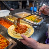 Koch serviert in einer Mensa ein veganes Gericht mit Nudeln und Soja-Bolognese (Archivbild)