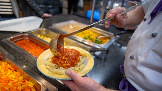 Koch serviert in einer Mensa ein veganes Gericht mit Nudeln und Soja-Bolognese (Archivbild)