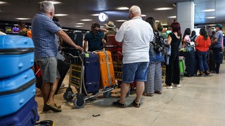Passagiere mit Gepäck stehen an einer Warteschlange im Flughafen
