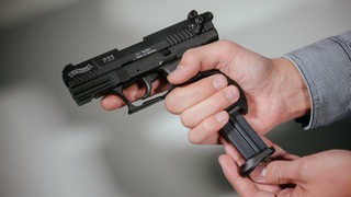 Hände laden eine Schreckschuss-Pistole "Walther P22" mit einem Magazin.