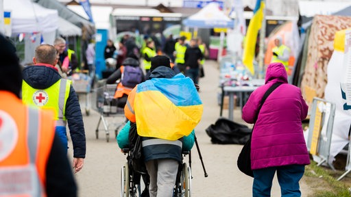 Ein Helfer mit ukrainischer Flagge um die Schultern schiebt am Grenzübergang Medyka kurz hinter der ukrainischen Grenze auf polnischer Seite eine Person im Rollstuhl.