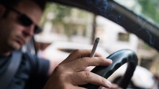 Ein Mann sitzt am Steuer seines Autos und raucht.