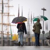 Spaziergänger mit Regenschirmen laufen an der Weserpromenade entlang. 