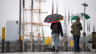 Spaziergänger mit Regenschirmen laufen an der Weserpromenade entlang. 