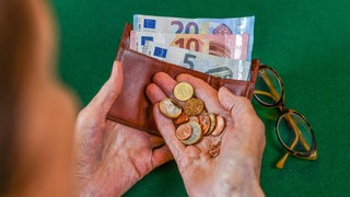 Eine ältere Frau blickt auf Münzen und ihren Geldbeutel in ihren Händen.