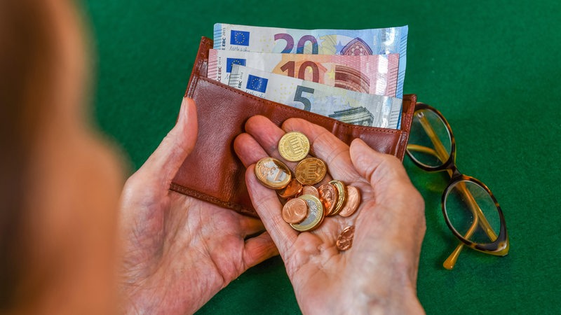 Eine ältere Frau blickt auf Münzen und ihren Geldbeutel in ihren Händen.