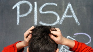 Ein Schüler rauft sich vor dem mit Kreide an eine Schultafel geschriebenen Wort PISA die Haare 