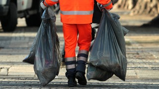 Ein Mitarbeiter eines Entsorgungsunternehmens trägt zwei Müllsäcke.
