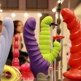 Verschiedene bunte Dildos werden auf einer Erotikmesse präsentiert.