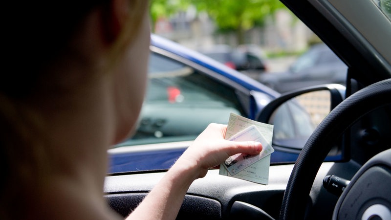 Eine Frau sitzt am Steuer eines Autos und hält Führerschein und Fahrzeugschein in der Hand.