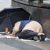 Eine obdachlose Person liegt schlafend auf dem Bürgersteig, eine Person läuft vorbei (Archivbild).