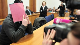 Der ehemalige Krankenpfleger Niels Högel versteckt sein Gesicht hinter einem Aktendeckel, während er am 19.02.2015 auf der Anklagebank des Landgerichts in Oldenburg (Niedersachsen) sitzt.