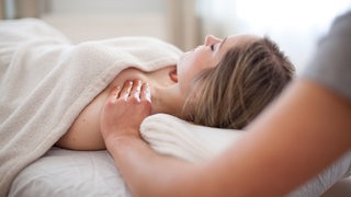 Eine Frau liegt auf einer Massagebank, ein Masseur hat die Hände an ihren Schultern.