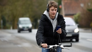 Ein Radfahrer mit Kopfhörern auf den Ohren und einem Handy in der Hand.