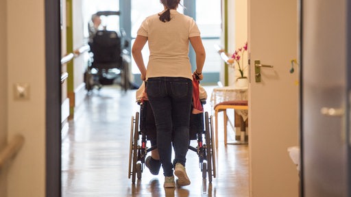 Eine Pflegerin schiebt einen Rollstuhl.