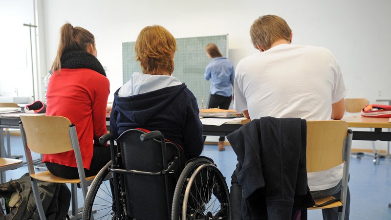 Drei Schüler im Klassenzimmer, einer im Rollstuhl