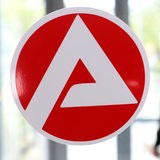 Das Symbol der Agentur für Arbeit klebt auf einer Glasscheibe. Dahinter sitzt ein Mensch.