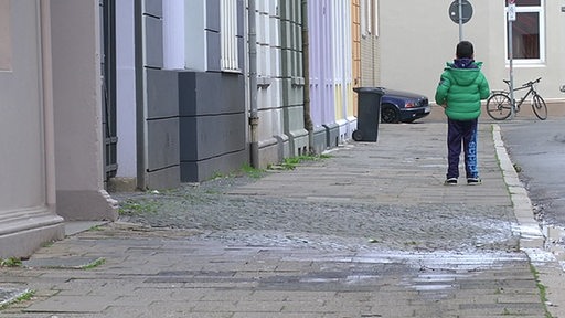Ein Kind von hinten, auf einem Gehweg