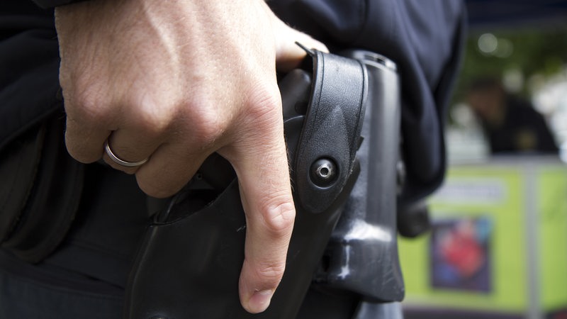 Die Hand eines Polizisten hält seine Dienstwaffe, die im Halfter hängt.