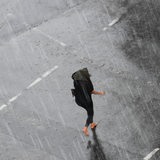 Eine Frau geht bei Regen mit einem Regenschirm über die Straße.