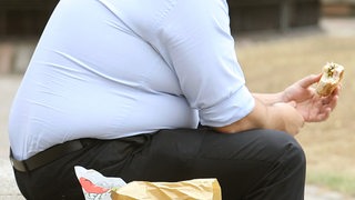 Ein übergewichtiger Mann sitzt auf einer Bank und isst Fastfood