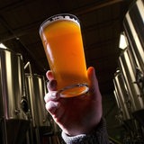 Ein Glas Craft Beer in einer Hand, vor mehreren Braukesseln.