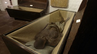Die mumifizierte Leiche von Oberst Gregor von Winsen liegt in einem dunklen Holzsarg im Bleikeller