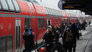 Reisende vor einem Zug auf einem Bahnsteig.