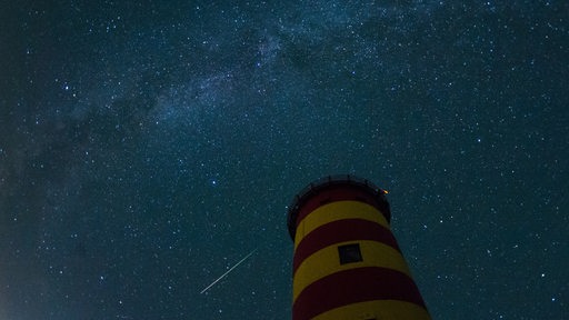 Ein Leuchtturm vor einem Nachthimmel mit Sternschnuppe.