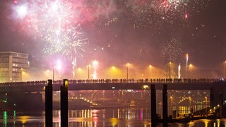 Menschen stehen auf einer Weserbrücke und sehen sich das Feuerwerk an.