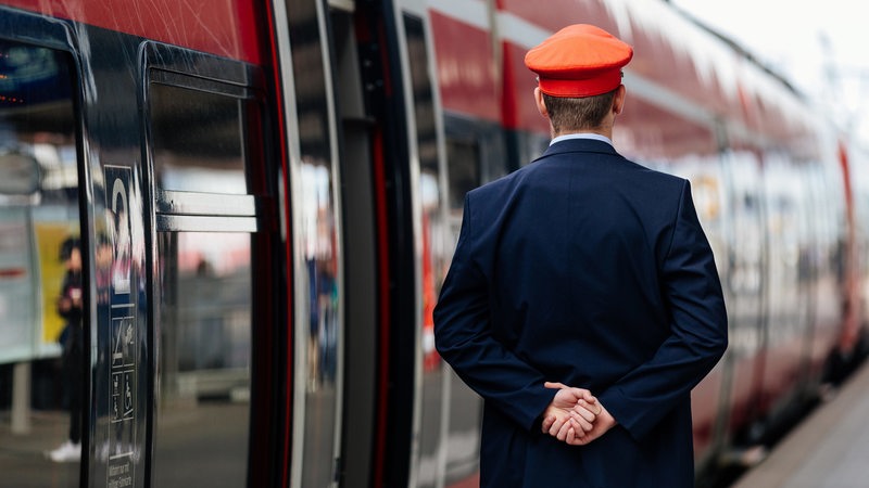 Ein Schaffner steht neben einem Regionalexpress.