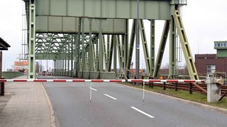 Eine Brücke mit riesigen Stahlträgern über der Straße, davor ist eine Schranke, die den Zugang zur Brücke versperrt.