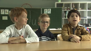 Drei Schulkinder sitzen an einem Tisch und diskutieren