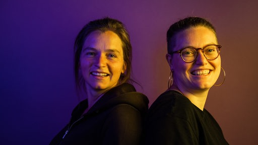 Zwei Frauen lächeln in lila-orangenem Licht für Foto in die Kamera